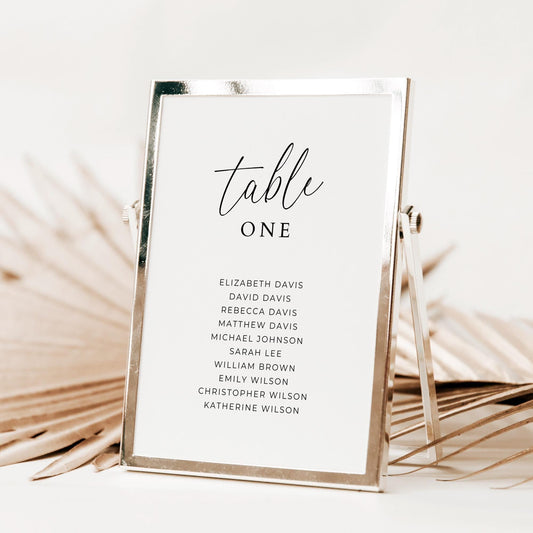 A table number card in a frame with the text &#39;table&#39; in a script font, followed by the number &#39;one&#39; and a list of 10 names.